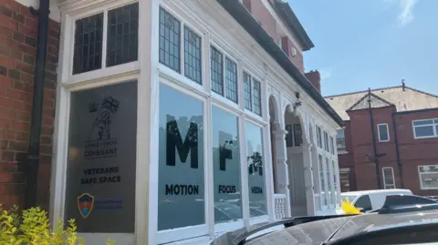 Bay windows at the front of a large property, with the words veterans safe space printed on the glass to the side