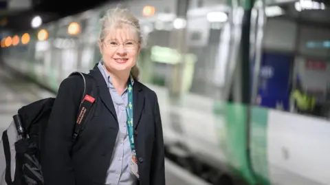 Peter Alvey Leigh Santamaria stood on a platform next to a train. She is wearing a black blazer and looking directly at the camera. 