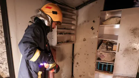 An emergency services responder wearing a helment and reflective jacket stands in a hair salon damaged in a strike in the occupied West Bank.