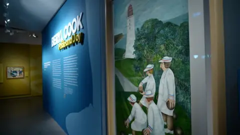 The title of the exhibition is written across a wall next to it is Beryl Cook's painting of women bowling on the Hoe.