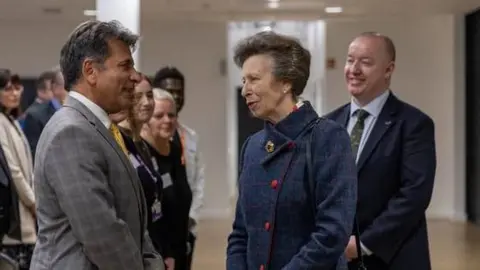Harper Adams University The Princess Royal meeting staff at the centre during an opening ceremony. She is wearking a blue coat with red buttons, and talking to a man in a line-up of guests.