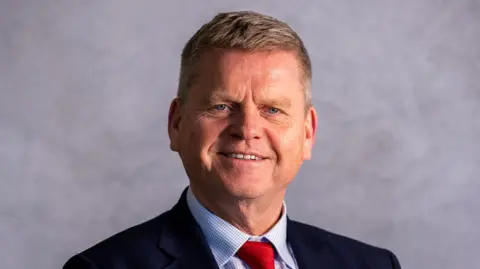 Reading University Prof Robert Van de Noort is wearing a dark suit, a blue and white shirt and a red tie 