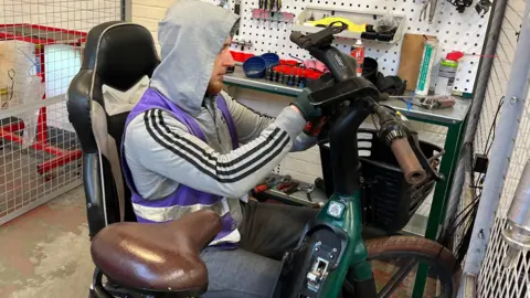 A worker in a grey hooded top is fixing the handlebars on an ebike
