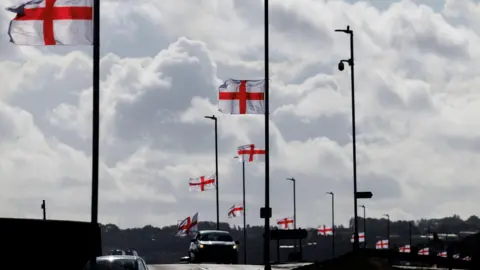 Getty Images A wide shot of a street with multiple lampposts with St George flags flying from them. A car is visible driving towards the camera