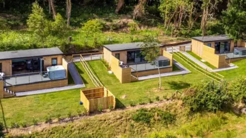 The image shows land with four luxury cabins situated there.