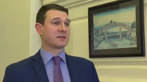 Man in blue suit and wearing a purple tie looking away from the camera 