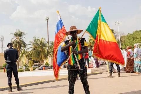 AFP A man holds two flags in his hands near the conference call - Russia's and Mali's.
