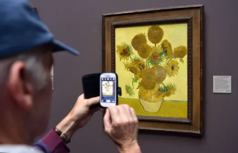 An audience member photographs the National Museum's version of Sunflowers by Vincent van Gogh