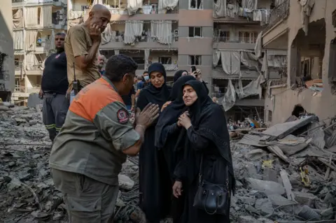 Joel Gunter/BBC Distraught residents speak to Youssef Al-Mallah, the head of the rescue team, at the site of the Basta strike.