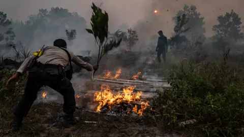 Getty Images A police officer attempts to extinguish a fire in Indonesia