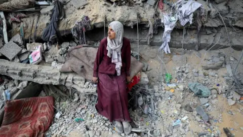 Reuters A Palestinian woman sits on the ledge of a heavily damaged building in Gaza