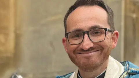 Jim Robinson, verger at Ipswich Minster, and Revd Tom Mumford, both dressed in Anglican church robes, stand outside St Mary-le-Tower church