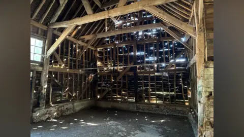 Katy Lewis/BBC An inside view of the barn shows a wooden structure and walls with holes between the planks and an earthy floor.
