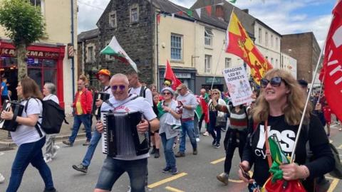 People marching for independence in a street in Bangor. may are holding Welsh national flags and wearing t-shirts with Yes Cymru printed on them.