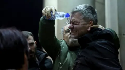 EPA-EFE/REX/Shutterstock A man pours water to help a protester after he was sprayed by police with pepper spray in Belgrade. Photo: 24 December 2023