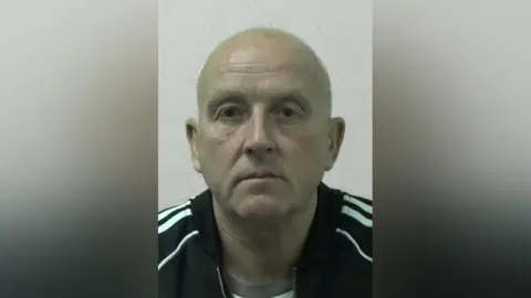 Michael Stewart's Northumbria Police Magshot. He is bald and clean shaved and wearing a black jacket