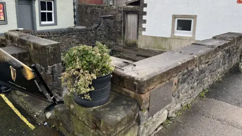 BBC News A stone well made up of two brick walls attached to a white building