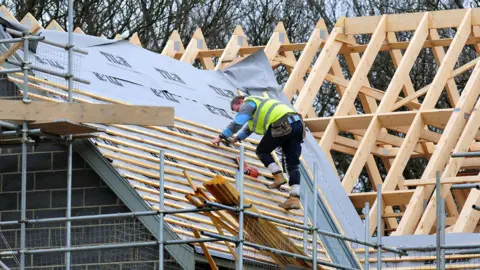 A roofer is wearing a high-res jacket and he is carrying out building work on the roof of a property. 