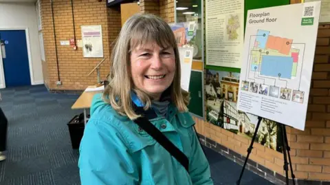 A woman with blonde hair. She is wearing a bright blue jacket. 
