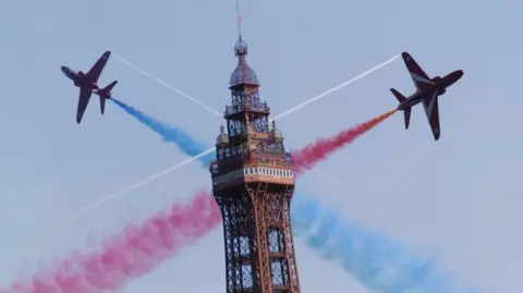 Two Red Arrows planes fly in opposite directions past over Blackpool Tower leaving red and blue smoke trails
