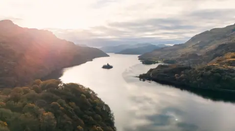 Getty Images A large loch surrounded by green trees with an island of greenery in the centre