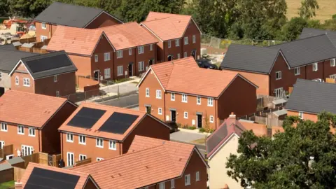 Steve Huntley/BBC An aerial picture of newly-built homes in Bacton. They are all made from red brick and have red or grey tiled roofs. Their white window frames are clearly seen in the sunshine. Three of the houses have solar panels visible and there are signs of construction work still going on.