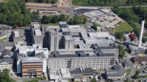 BBC Aerial view of Derriford Hospital, the hospital's helipad is in the upper right with a white cross and a yellow circle around it