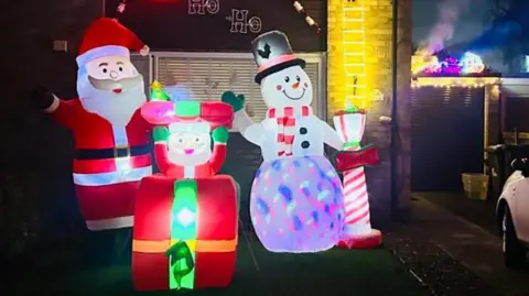 Jason Fletcher A colourful outdoor Christmas display with an inflatable Santa, snowman, and a smaller Santa popping out of a present.