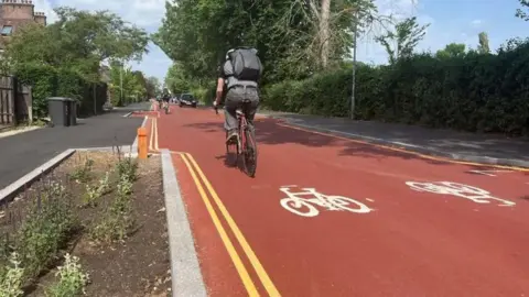 Man in black jeans and grey shirt rides a red bicycle on new red tarmac cyle road