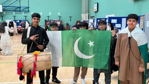Shariqua Ahmed Four boys posing with the Pakistan flag smiling at the camera