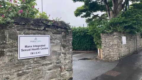 BBC The entrance to the Manx Integrated Sexual Health Centre. The are stone walls either side of the entrance and a white sign on the left.