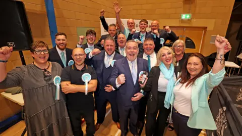 LDRS People in suits and pale blue rosettes with hands in their air celebrate
