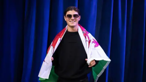 Getty Images Rees-Zammit poses with the flag of Wales during the NFL Draft in April