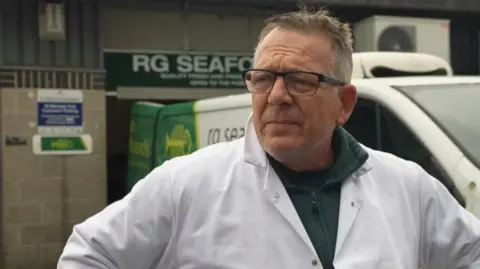 Rob Goodacre wearing a white lab coat and green jumper looks to the left of the camera