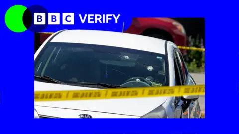 A white car with bullet holes through the window, surrounded by police tape. There is blue and green BBC Verify branding in the top left corner. 