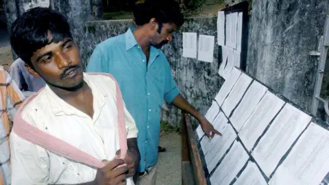 Indian villagers check the list of missing persons at a relief camp in Port Blair, capital of India's Andaman and Nicobar Islands, December 31, 2004. Indian tsunami survivors are desperately trying to track down their missing relatives as relief workers in the Andaman Islands. It was difficult to unite the family separated by the ordeal.