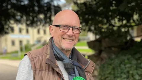 Martin Dimery Martin Dimery with a green rosette in a park.