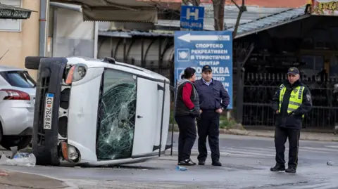 Reuters Um carro danificado é visto em uma rua durante um protesto após um incêndio no clube que resultou em dezenas de mortes, na cidade de Kocani, norte da Macedônia, 17 de março de 2025