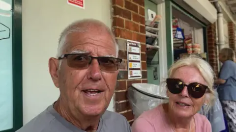 Robin Grey / BBC A man and a woman sat outside a train station.