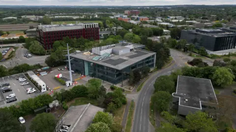 Steve Hubbard/BBC An aerial image of Cambridge Science Park. There are several large, modern buildings with a lot of glass. One of them, which is in the middle, is the Aveva building which is three storeys high and has a car park outside the front.