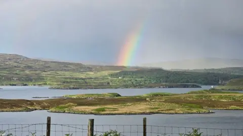 The water has lots of little islands and a rainbow can be seen on a cloud in the distance.