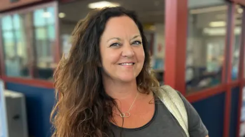 Zoe Gosling is standing in front of the Duty Free section of the ferry departure terminal. She is smiling at the camera.