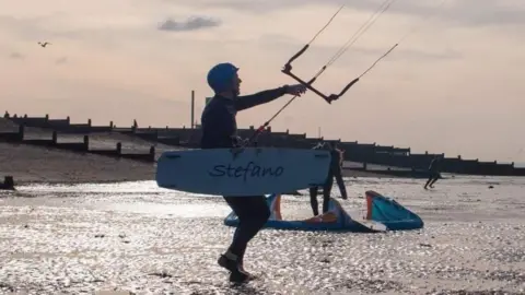 Andrew Hastings A kitesurfer is on a sandy beach in silhouette. 