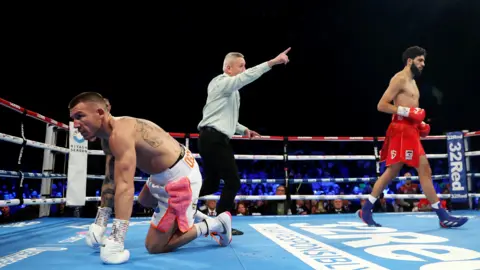 Liam Williams on his knees as the referee orders Hamzah Sheeraz back to his corner