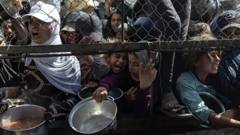EPA Displaced Palestinians gather outside a charity kitchen for food, in Khan Younis, southern Gaza (30 May 2025)