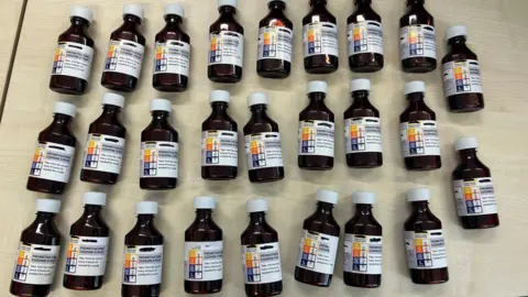 Rows of small brown medicine bottles with white caps laid out on a table.
