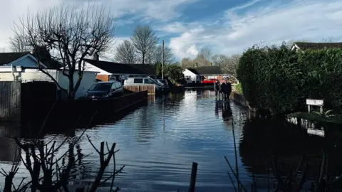Flooded street at Winterborne Kingston in Dorset. People are seen walking through the water.