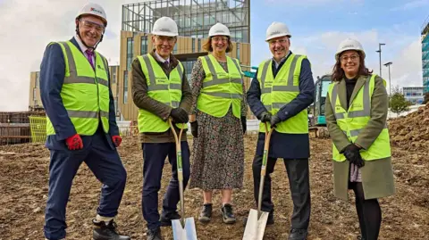 University of Huddersfield Kier Construction's Daniel Doherty, Professor Tim Thornton, Professor Jane Owen-Lynch, chief executive of Calderdale and Huddersfield NHS Trust Brendan Brown and Huddersfield MP Harpreet Uppal wearing high-vis jackets and holding spades.