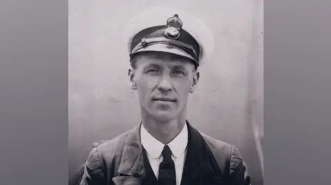 Noonans A black and white image of Chief Petty Officer Reginald Vincent Ellingworth. He is wearing Royal Navy uniform including a badged, peaked cap, white shirt, dark tie and jacket. He is wearing three medals on his left breast with naval stripes on his left jacket arm. 
