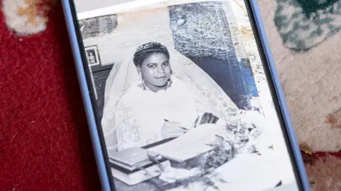 Steve Reeves A phone with a black and white picture on the screen of a woman in a wedding dress and veil, signing a marriage register 